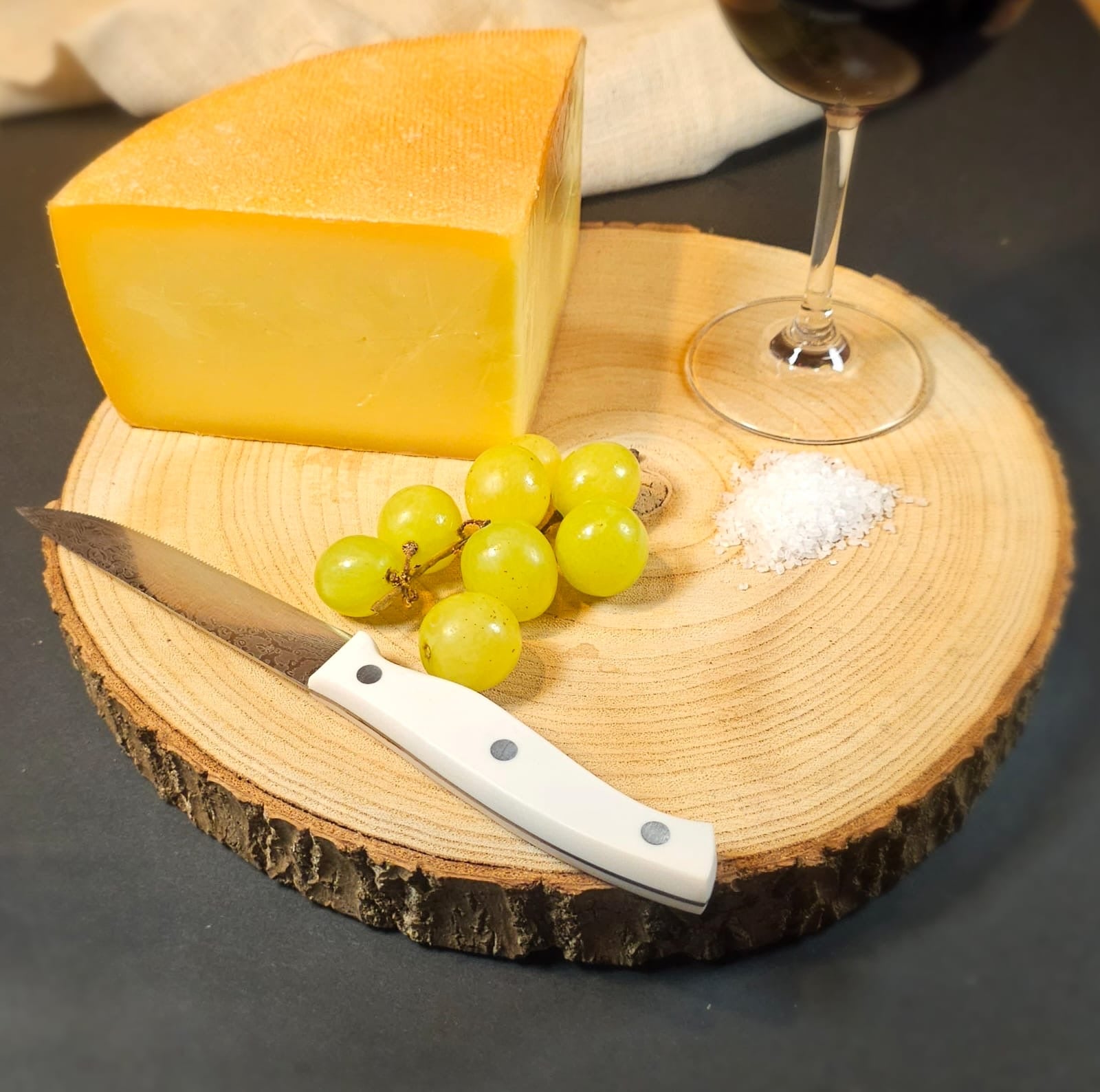 Ein Stück würzig Zillertaler, Bergkäse aus Heumilch mit einem Brett, Weintrauben, einem Messer und einem Glas Rotwein