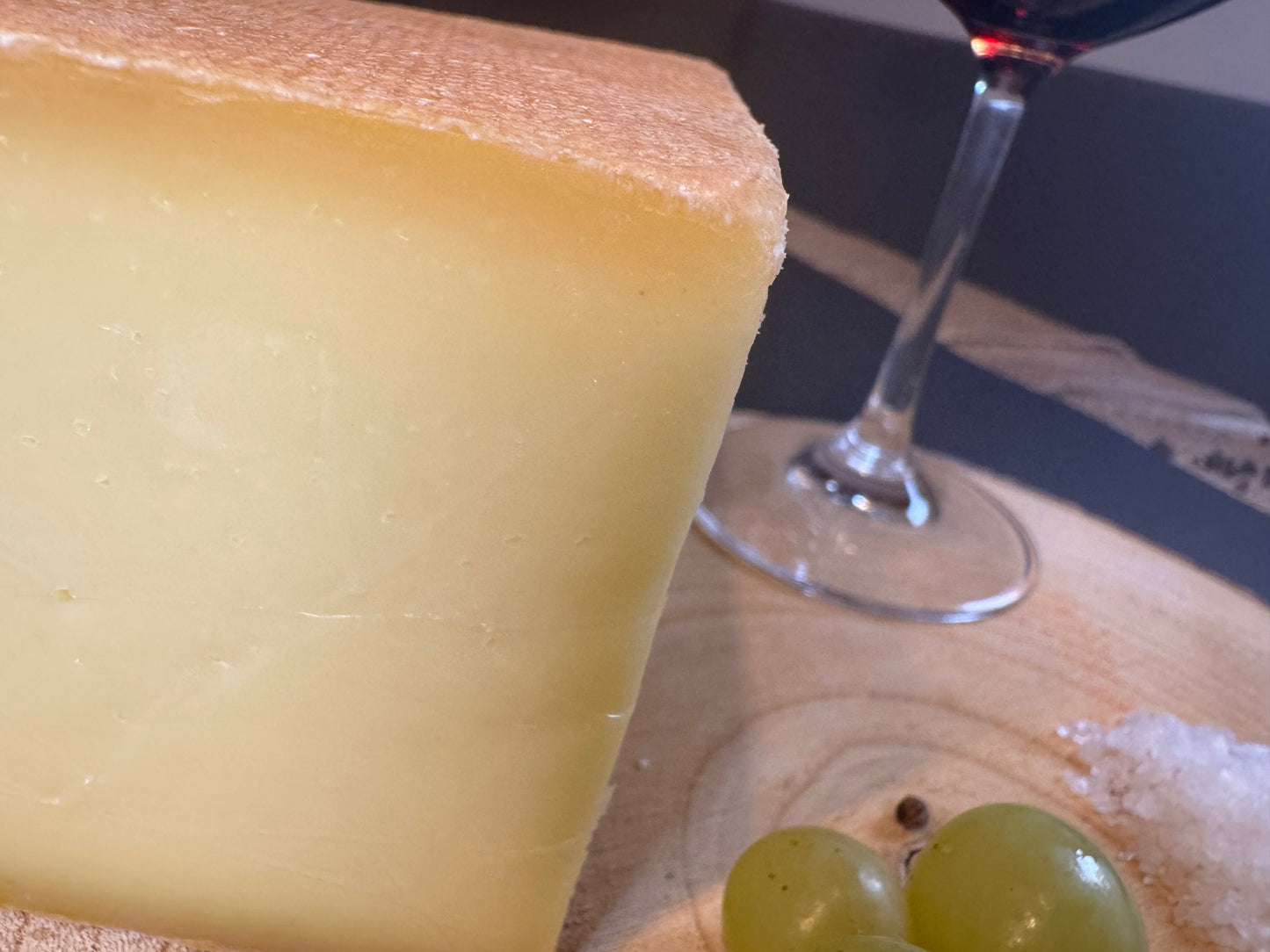 Bergkäse würzig, Nahaufnahme mit einem Glas Wein und ein paar Weintrauben