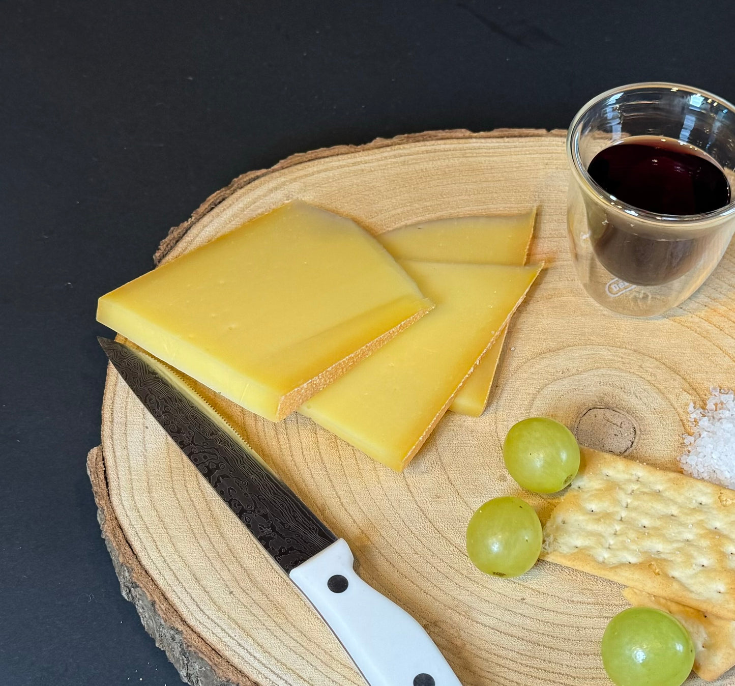 Bergkäse, würzig, in Scheiben, aufgeschnitten, Glas Wein, ein paar Weintrauben und ein paar Cracker