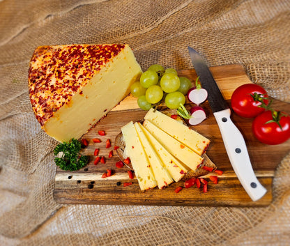 Bergkäse, Brotzeit,brett mit Chili verfeinert aufgeschnitten mit ein paar Weintrauben und einem Küchenmesser. Schön dekoriert und angerichtet mit Tomaten und Petersilie.