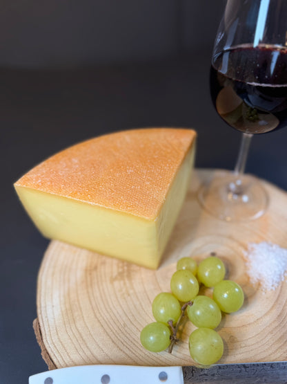 Holzbrett dekoriert mit einem Glas Wein, ein paar Weintrauben, einem Haufen Grobkönigen Meersalz und einem Bergkäse