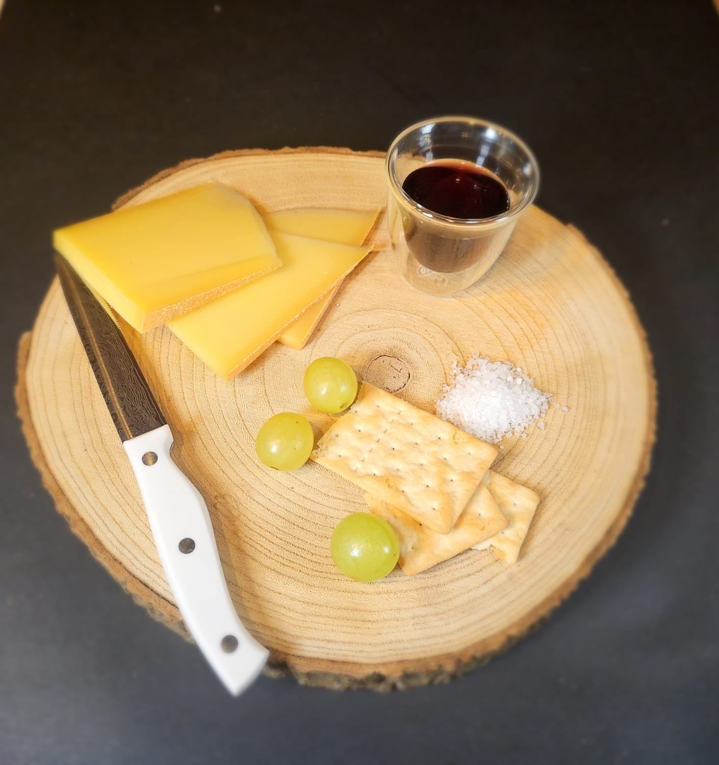 Bergkäse in Scheiben geschnitten, wieder ein paar Cracker und Weintrauben mit einem Glas Rotwein